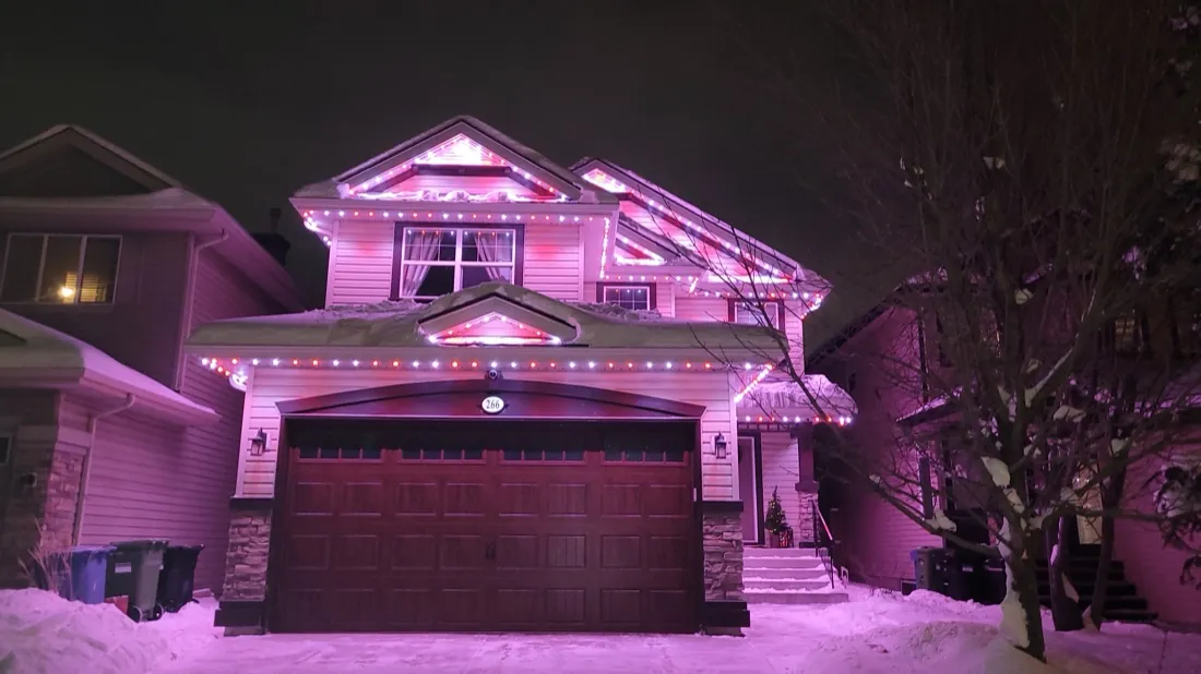 Snow-covered Calgary home lit in festive permanent LED colours on a winter night