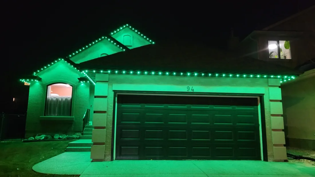 Calgary home displaying vivid green permanent LED lighting across the roofline and garage at night