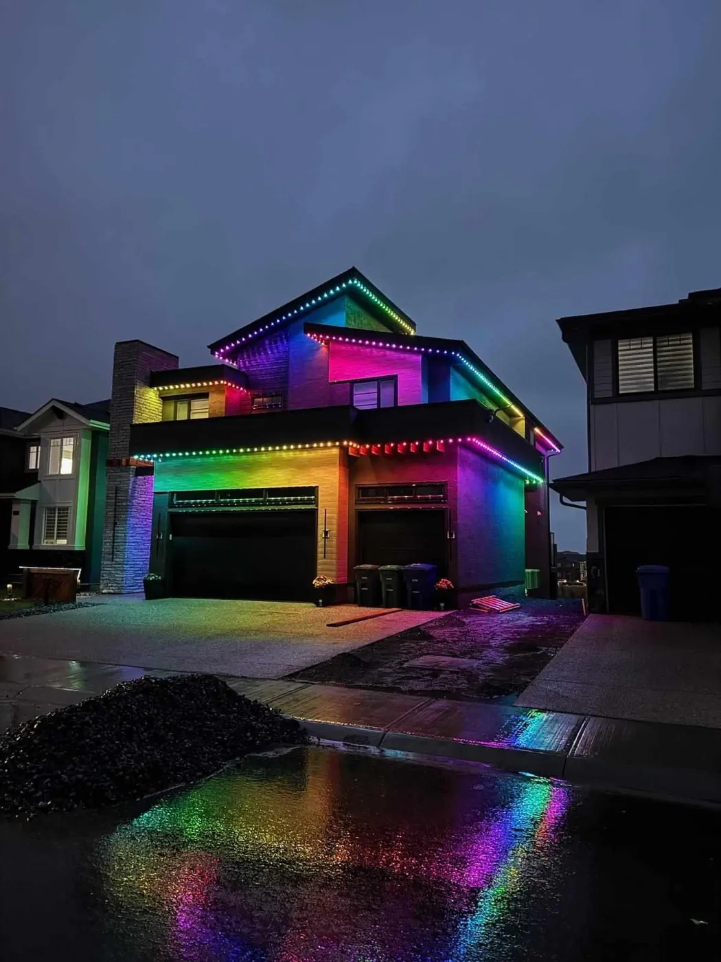 Calgary home lit in full multicolour permanent LED lighting reflected on a wet driveway at night