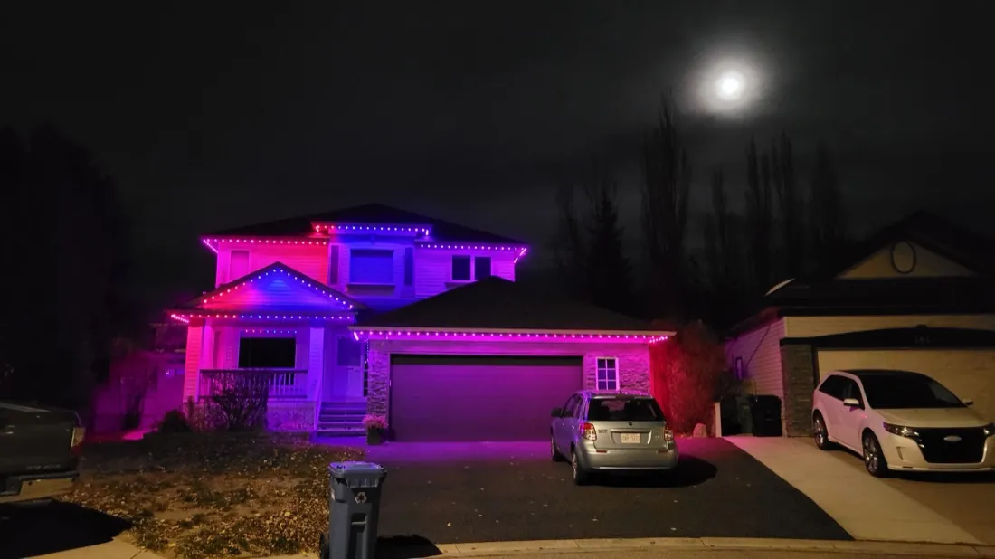 Calgary home glowing pink with permanent LED lighting under a moonlit winter sky