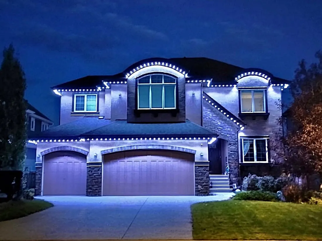 Calgary home with crisp white permanent LED trim outlining the roofline and double garage arches at night