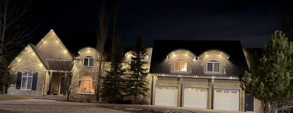 Wide night view of a Calgary home with warm white permanent LED lights along the roof peaks and garages